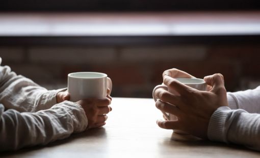 two people facing each other with coffee cups