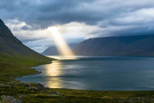 Light shining through clouds onto lake surrounded by mountains