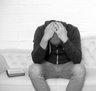 Greyscale image of an individual sitting on a couch with his hands on his head