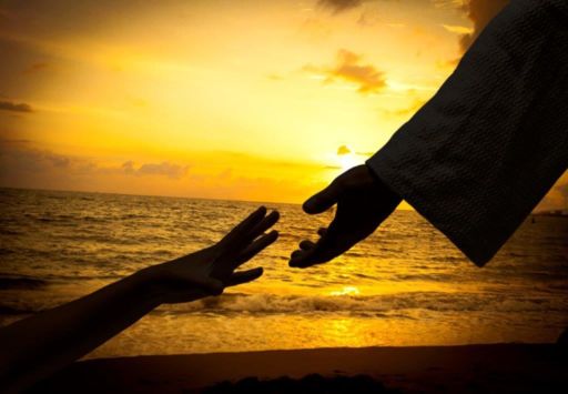 Silhouette of outstretched hand with other hand reaching on the beach at sunset