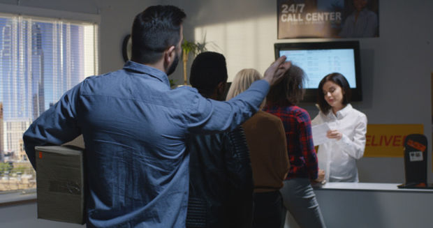 People standing in line with the last person making a gesture towards the front of the line