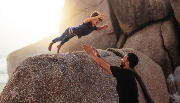 Child jumping off a boulder into a father's arms