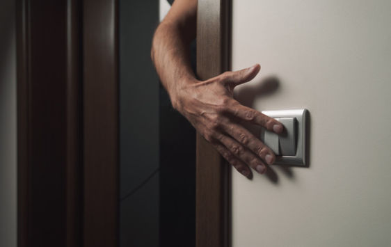 Person's hand reaching around the corner to flip a light switch