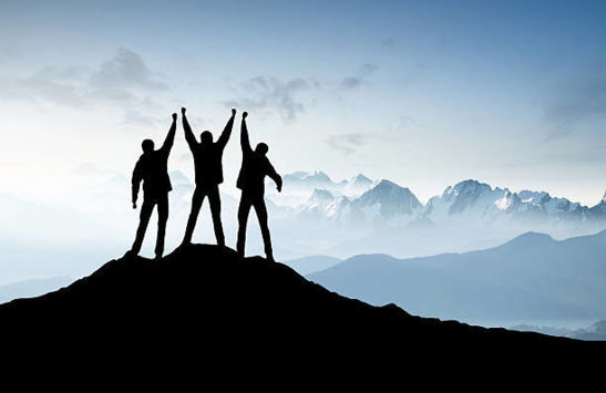 Silhouette of 3 people at the top of a mountain with hands in the air 