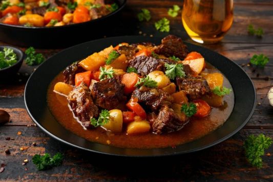 Stew with potatoes, carrots and beef on a black plate