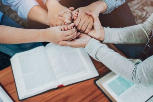 Bibles on table with arms stretched out holding hands overtop