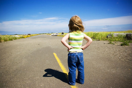 Young child with hands on hips on a road looking towards the open sky and fields