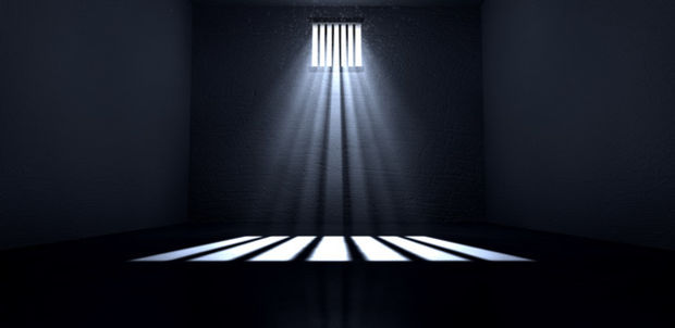 Dark cell with only light coming through a barred window and reflecting on the ground