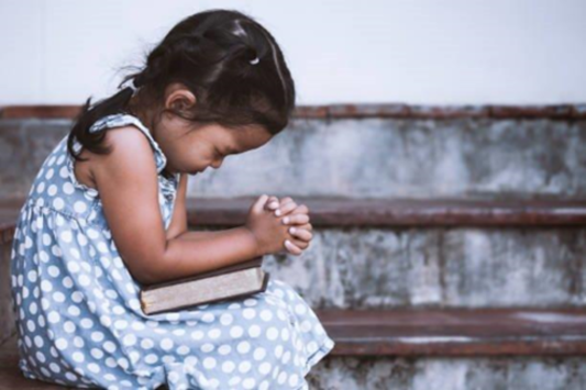 Young Child with book in lap and clasped hands praying