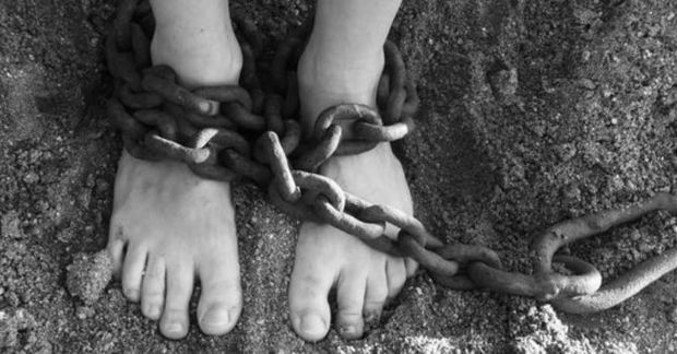 Greyscale image of a person's feet in sand or dirt with chains wrapping around